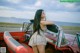 A woman leaning on the hood of a red convertible car.