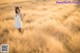 A woman in a white dress standing in a field of tall grass.